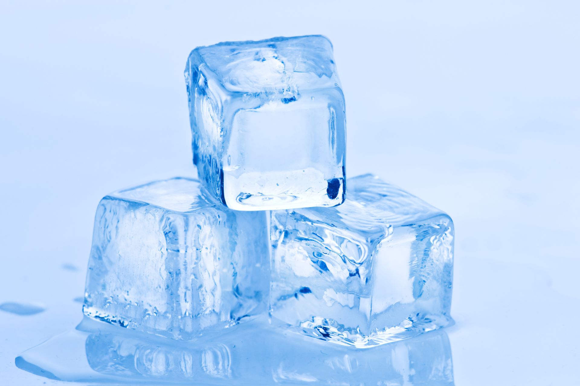 Three crystal-clear ice cubes stacked on a glossy blue surface with melting water and soft reflective highlights.
